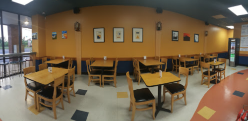 A spacious restaurant interior with wooden tables and chairs, orange walls, and framed artwork.
