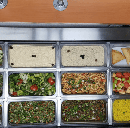 A variety of colorful dishes including hummus, salads, and samosas in a stainless steel food display.