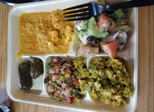 A divided plate with various dishes: lentil curry, salad, mixed beans, spiced greens, and a stuffed grape leaf.