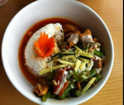 A bowl of rice topped with chicken, green beans, and garnished with ginger and a decorative carrot flower.