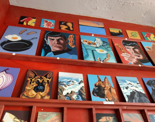 A colorful wall display featuring various paintings, including a dog, food items, and a character resembling Spock.