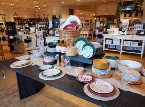 A display of colorful dinnerware and kitchen items arranged on a wooden table in a home goods store.