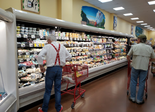 Two shoppers in a grocery store aisle filled with various dairy products, one wearing red suspenders.