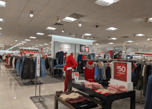 A retail store interior featuring clothing racks, a display table with sweaters, and a sign for $50 and under items.