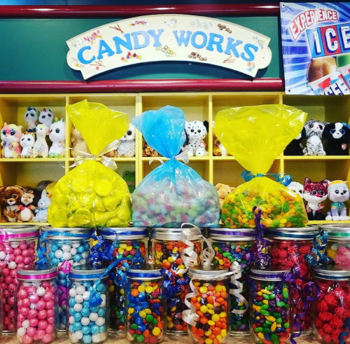 Colorful candy bags and jars filled with various candies, displayed in a cheerful candy shop setting.