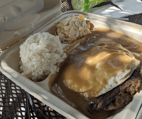 A takeout container with rice, a hamburger patty topped with gravy and an egg, and a side of pasta salad.