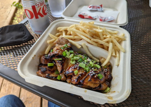 A takeout container with grilled chicken topped with green onions and sesame seeds, served with fries and a Diet Coke.