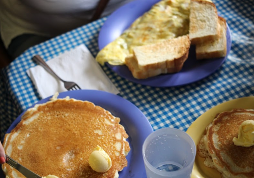 A table set with pancakes topped with butter, an omelet, and slices of toast on a blue checkered tablecloth.