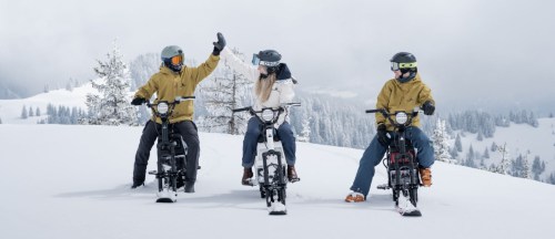 Three people on electric bikes in a snowy landscape, wearing winter gear and helmets, enjoying the winter scenery.