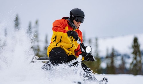 A person in a bright yellow and red jacket skiing on a snowy slope, creating a spray of snow.
