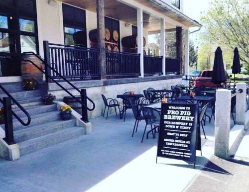 Outdoor seating area at Pro Pig Brewery, featuring tables, umbrellas, and a welcoming sign.