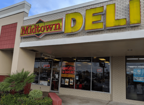 Exterior of Midtown Deli with a bright sign, showcasing "Open" and "Bagels & Bread" in the window.