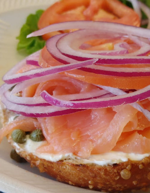 A bagel topped with cream cheese, smoked salmon, red onion, tomato slices, and capers on a plate.