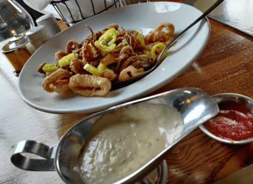 A plate of fried calamari with green peppers, accompanied by a bowl of creamy dipping sauce and a small dish of red sauce.