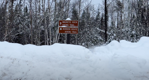 Signpost for Magnetic Rock and Border Route hiking trails, surrounded by snow-covered trees in a winter landscape.