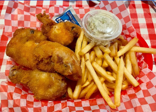 A basket of fried chicken pieces, French fries, and a small container of coleslaw on a red and white checkered paper.