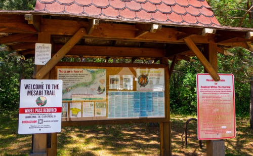 Information kiosk at the Mesabi Trail with maps and guidelines, surrounded by trees. Signs indicate trail access and rules.