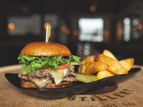 A juicy burger with lettuce, tomato, and cheese, served with golden potato wedges on a black plate.