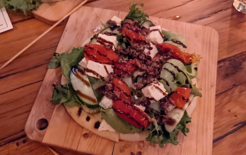 A wooden board topped with a fresh salad of greens, cucumbers, feta cheese, and drizzled with balsamic glaze.