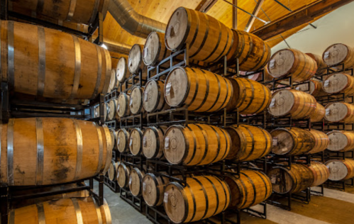 A spacious warehouse filled with stacked wooden barrels on metal racks, showcasing a rustic, industrial atmosphere.