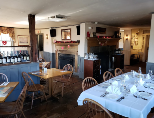 Cozy restaurant interior with wooden tables, a fireplace, and wine bottles on display, decorated for a festive occasion.