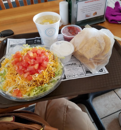 A salad with lettuce, cheese, and tomatoes, accompanied by cookies, salsa, and a drink on a tray.