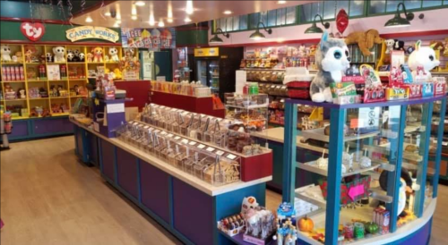 A colorful candy store interior filled with shelves of sweets, toys, and plush animals.