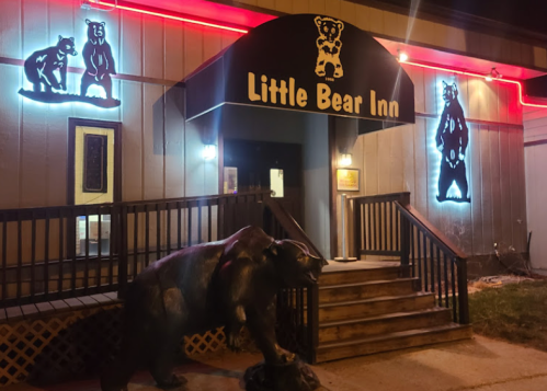Exterior of the Little Bear Inn at night, featuring bear-themed decorations and a bear statue at the entrance.