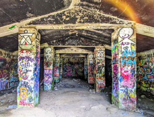 Graffiti-covered pillars inside a dark, abandoned structure with a rocky floor and a ceiling overhead.