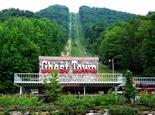 A rustic building with "Ghost Town" sign in front of a green mountain and ski lift in the background.