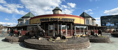 Exterior of Wood Grill Buffet restaurant with a circular design, surrounded by landscaping and animal sculptures under a blue sky.
