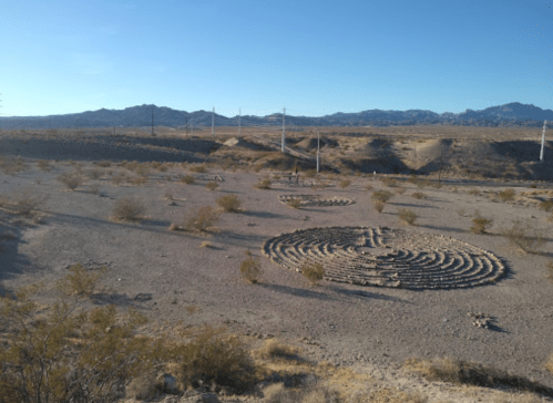 Aerial view of stone labyrinths in a desert landscape, surrounded by sparse vegetation and distant mountains.