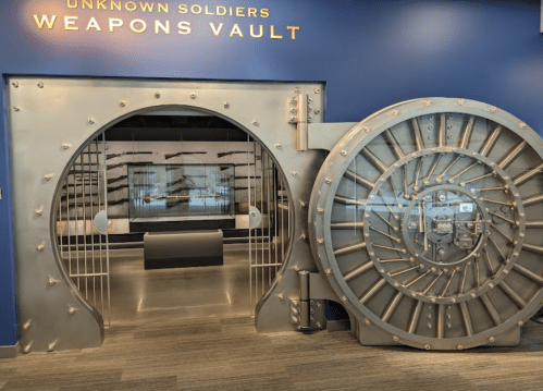 A large vault door labeled "Weapons Vault" with a metal design, leading to a display area.
