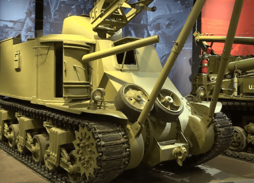 A military vehicle with a yellow exterior, featuring tracks and a raised arm, displayed in a museum setting.