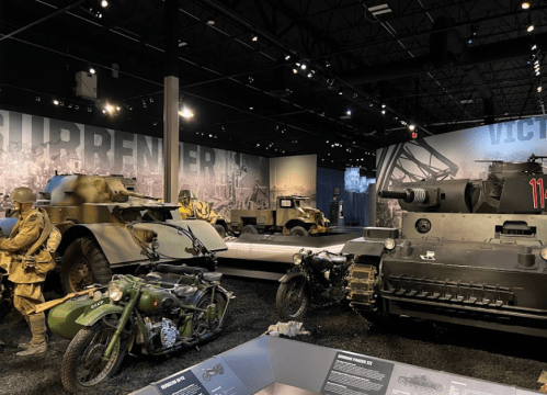 A military exhibit featuring tanks, armored vehicles, and soldiers' uniforms in a dimly lit museum setting.