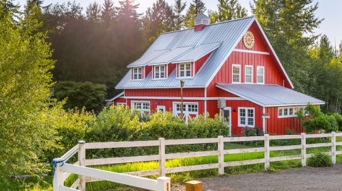 A charming red barn-style house surrounded by greenery and a white fence under a sunny sky.