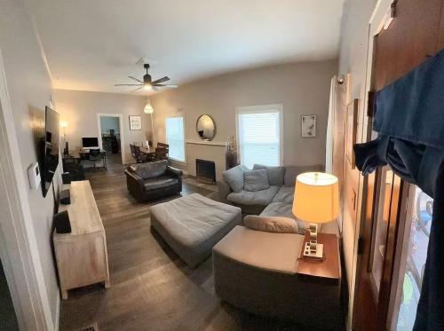 Cozy living room with a sectional sofa, armchair, lamp, and dining area in the background. Bright and inviting atmosphere.