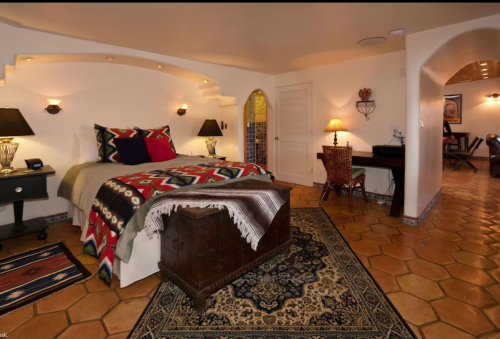Cozy bedroom with a patterned bedspread, wooden trunk, and warm lighting, featuring terracotta tile flooring.