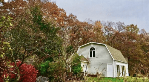 A charming gray house surrounded by colorful autumn trees and foliage.