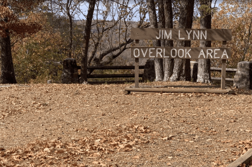 Sign for "Jim Lynn Overlook Area" in a wooded setting with fallen leaves and trees in the background.