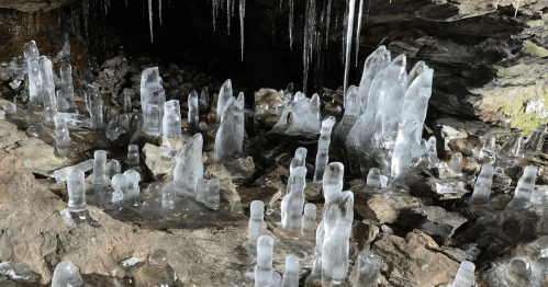 Ice formations resembling stalagmites in a rocky cave, with icicles hanging from the ceiling above.