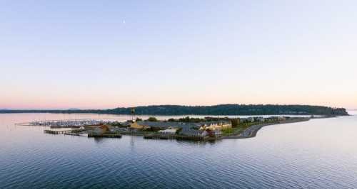 A serene waterfront view of a marina and coastal village at sunset, with calm waters and distant hills.