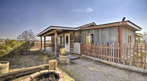 A rustic house with a wooden porch, surrounded by a picket fence and desert landscaping under a clear blue sky.