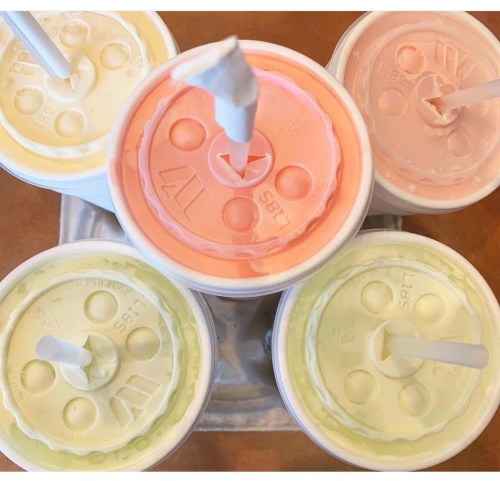 Five colorful drink cups with lids and straws arranged in a circle on a tray.