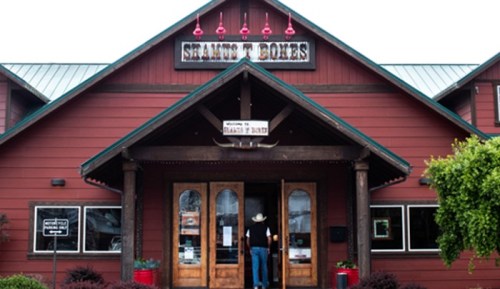 A person enters a rustic red building with a sign reading "Steamboat Bones" and welcoming decor.