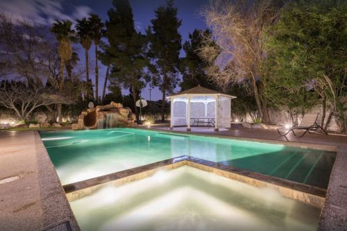 A serene pool area at night, featuring a gazebo, palm trees, and soft lighting around the water.