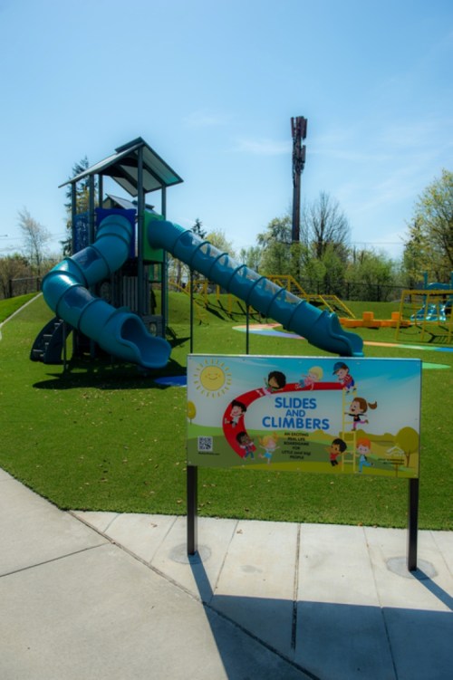A colorful playground featuring a large blue slide and a sign that reads "Slides & Climbers" on a sunny day.
