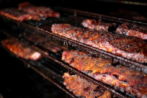 Close-up of smoky, grilled ribs on a rack, showcasing a charred, flavorful exterior.