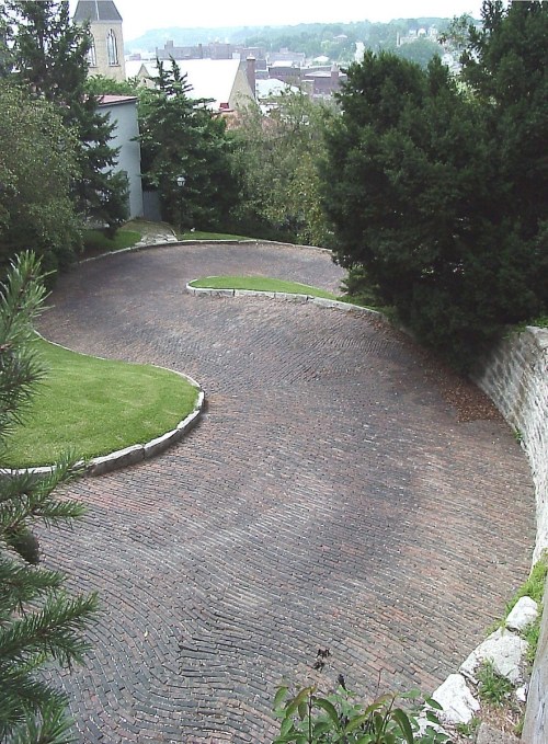 A winding brick pathway surrounded by greenery and trees, leading to a scenic view in the background.
