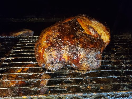 A close-up of a smoked, seasoned piece of meat resting on a grill, showcasing a dark, crispy exterior.